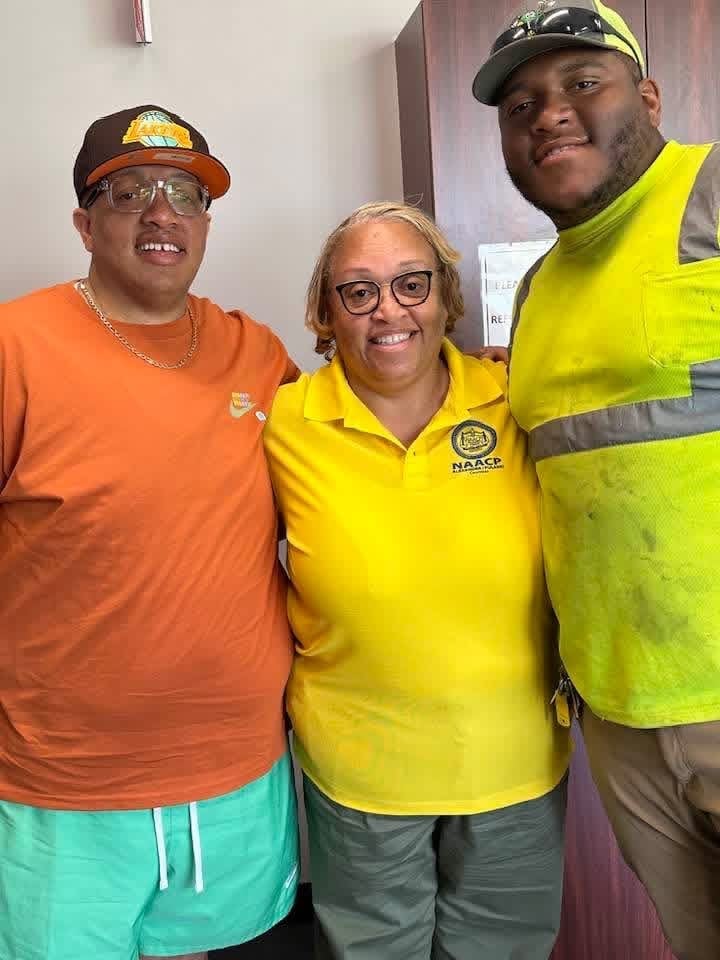 Three smiling workers posing together indoors wearing safety gear and orange, yellow, and neon yellow clothing