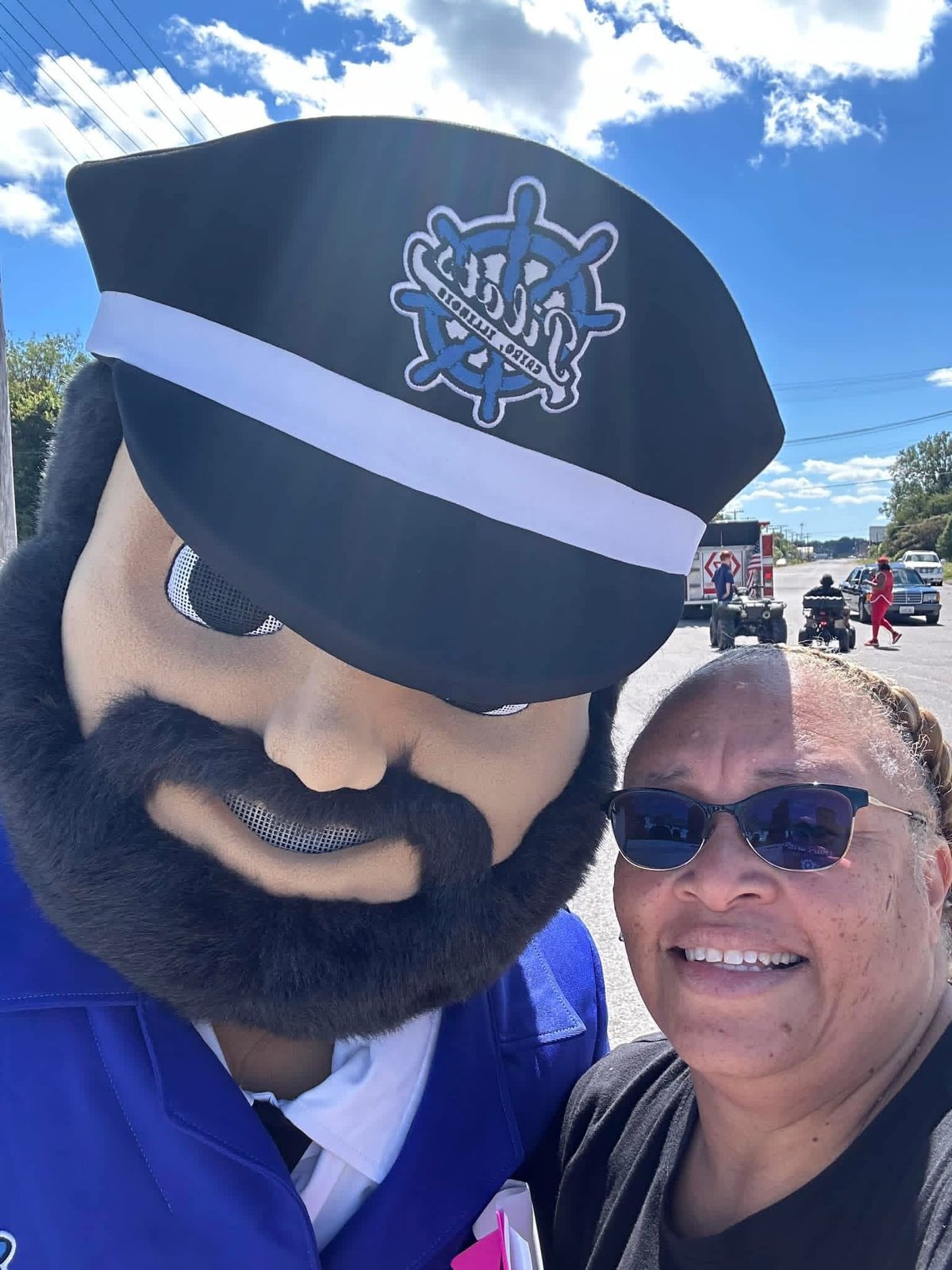 Artie McBride in sunglasses smiling next to a costumed sea captain mascot with a ships wheel logo on his hat