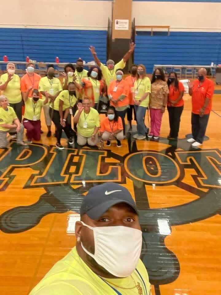Group of people wearing yellow and orange shirts standing in a school gymnasium during a community event