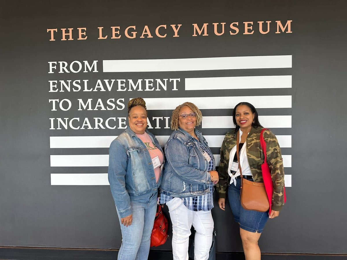 Three people standing in front of The Legacy Museum wall display about enslavement and mass incarceration