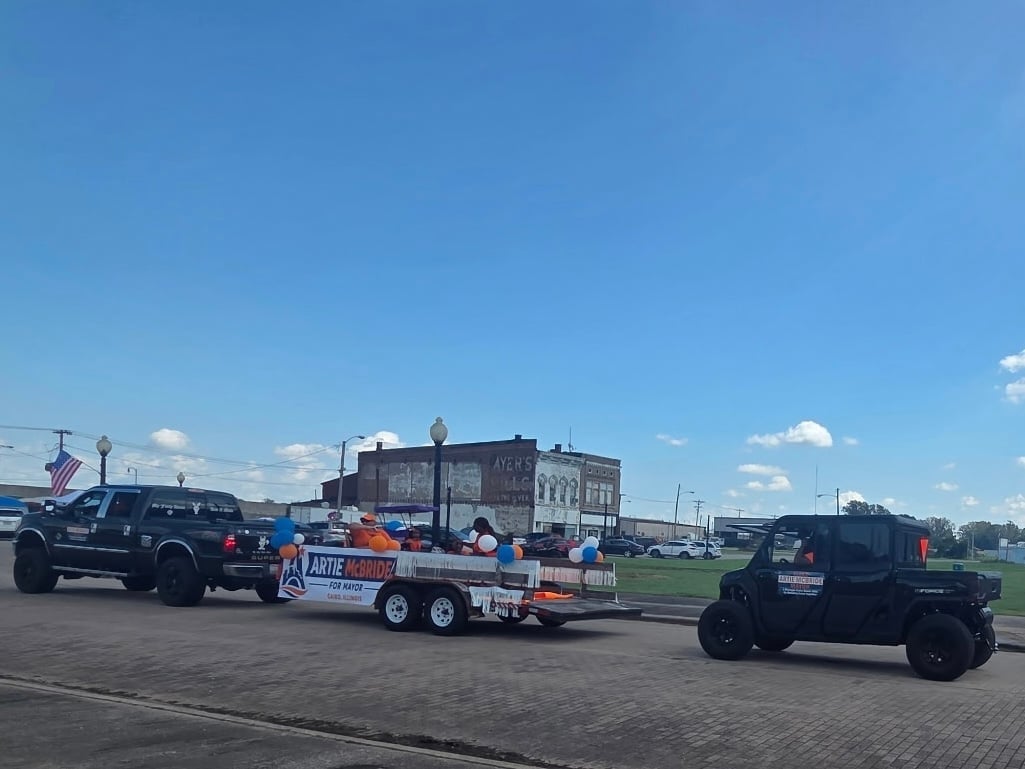 Modified Jeeps and a custom campaign trailer parked outdoors at the Cairo Heritage Blues Fest under a clear blue sky