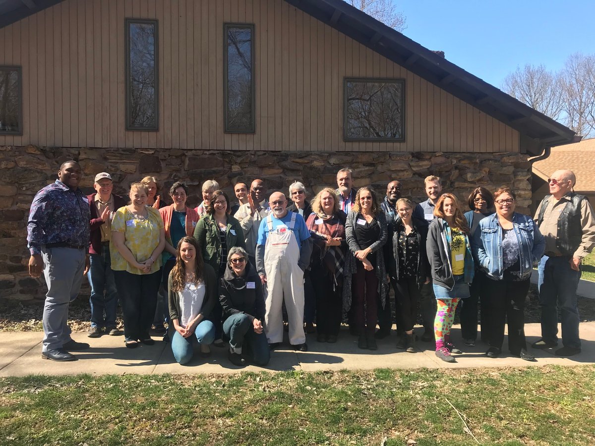 Large group of people posing together outside a modern barn building on a sunny day